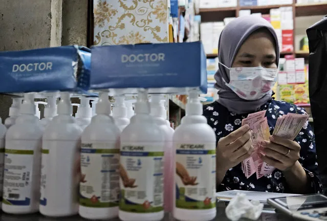 A cashier counts money behind bottles of hand sanitizers at a medical supply shop in Jakarta, Indonesia, Wednesday, March 4, 2020. Indonesia confirmed its first cases of the coronavirus Monday in two people who contracted the illness from a foreign traveler. (Photo by Dita Alangkara/AP Photo)