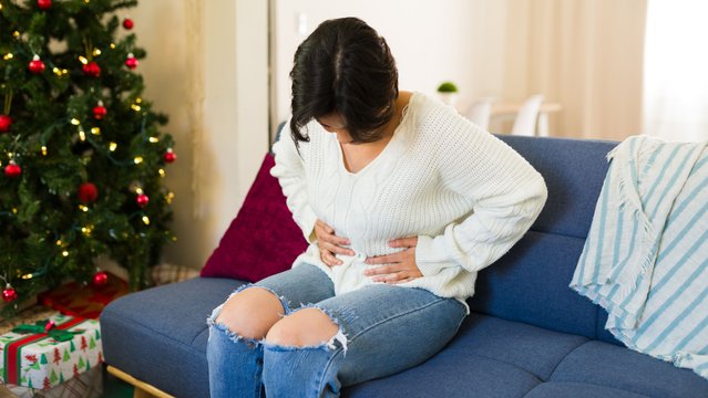 Young woman suffering from a stomach ache while relaxing on a couch at home over the christmas break. (Photo by Antonio Diaz/Getty Images)