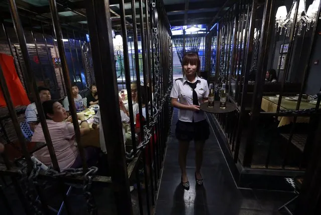 A waitress poses while customers eat dinner inside iron cages at a jail-themed restaurant in the Chinese port city of Tianjin September 9, 2014. The three-story restaurant consists of rooms resembling jail's cells made from iron caging and it attracts customers who wants to experience the atmosphere of the jail for fun. (Photo by Kim Kyung-Hoon/Reuters)