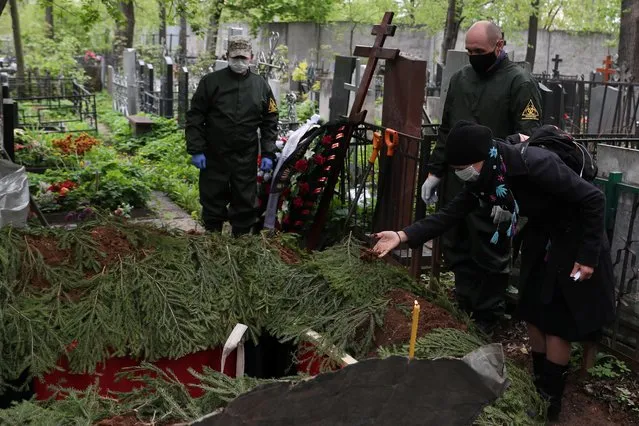 A mourner wearing a protective face mask throws ground into the grave of Orthodox deacon Andrei Molchanov, 54, who died after contracting the coronavirus disease (COVID-19), during a funeral at a cemetery in Moscow, Russia on May 9, 2020. (Photo by Evgenia Novozhenina/Reuters)