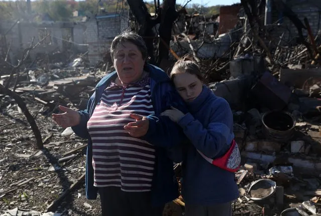 A girl and her grandmother, local residents, react as they stand outside a house destroyed as a result of shelling in town in Kupiansk, Kharkiv region on October 17, 2022, as the Russia-Ukraine war enters its 236th day. (Photo by Anatolii Stepanov/AFP Photo)