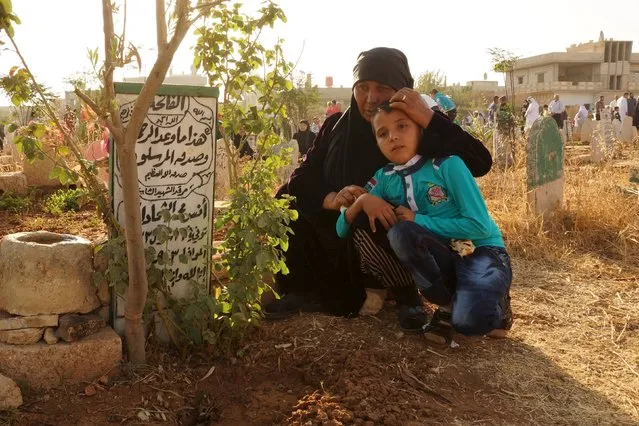 A woman holds her grandson as she prays near her son's grave at the Martyrs' cemetery on the first day of Eid al-Adha in the town of Dael near Deraa, Syria September 24, 2015. (Photo by Alaa Al-Faqir/Reuters)