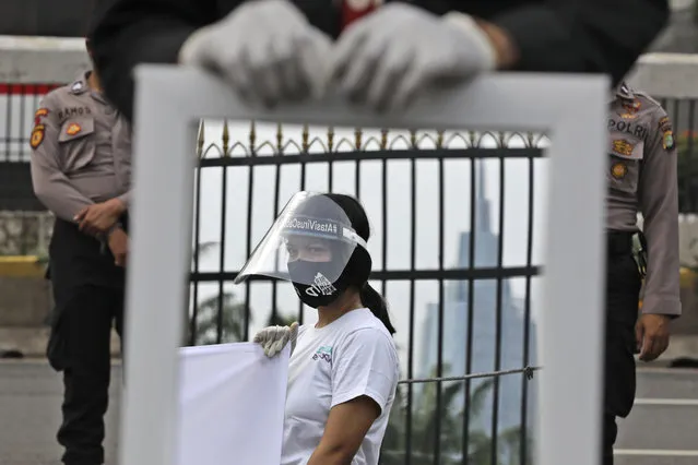 A mirror reflects the image of an activist wearing a mask and protective face shield as a precaution against the new coronavirus outbreak during a small protest outside the parliament in Jakarta, Indonesia, Tuesday, July 14, 2020. About a dozen activists staged the protest opposing the government's omnibus bill on job creation that was intended to boost economic growth and create jobs, saying that it undermined labor rights and environmental protection. (Photo by Dita Alangkara/AP Photo)