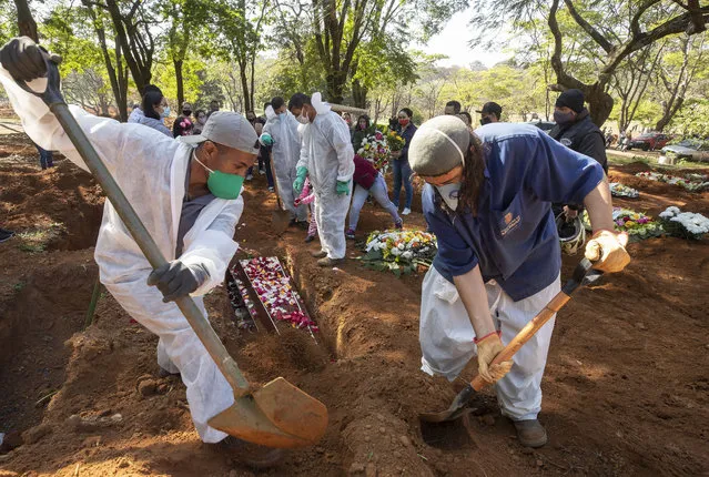 Cemetery workers bury 65-year-old Maria Joana Nascimento, whose family members, behind, suspect died of COVID-19, at Vila Formosa cemetery in Sao Paulo, Brazil, Thursday, August 6, 2020. Brazil is nearing 3 million cases of COVID-19 and 100,000 deaths. (Photo by Andre Penner/AP Photo)