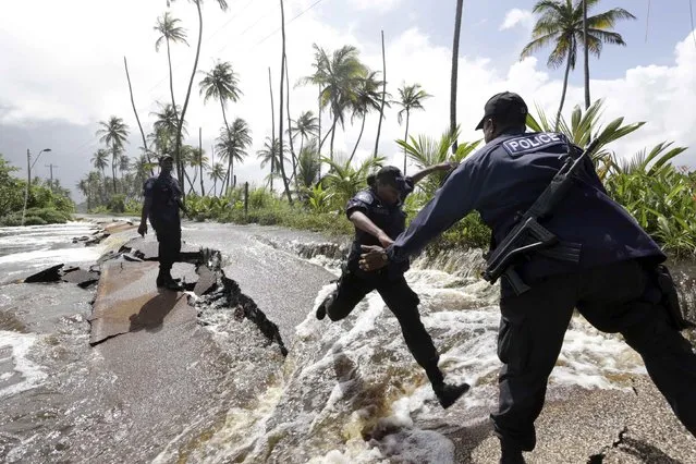 Police Constable Patrice Clarke jumps over a collapsed portion of Manzanilla Mayaro Road, as flood waters continue to flow from the adjoining Nariva swamp basin following two days of rainfall in the country, in Manzanilla on Trinidad's East coast November 17, 2014. According to local authorities, more than 80 per cent of the road has been submerged by over a foot of water for the past two days, destroying the road's surface as it roars to the seafront. (Photo by Andrea De Silva/Reuters)