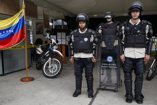 Venezuela's national police officers Bello (R) and Bogado pose for a picture with their riot equipment, next to a mannequin in uniform during a government Christmas fair in Caracas November 13, 2014. In Venezuela, no firearms are to be carried or used for control of peaceful demonstrations. When there is a threat to order, and other methods of conflict resolution have failed, police are instructed to warn crowds or demonstrators that there will be a “progressive, differentiated use of force”. (Photo by Carlos Garcia Rawlins/Reuters)