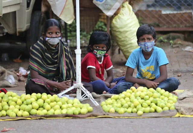 An Indian woman selling lemons sits with her children wearing face masks as a precaution against the coronavirus as they wait for buyers in Bengaluru, India, Sunday, October 11, 2020. India's confirmed coronavirus toll crossed 7 million on Sunday with a number of new cases dipping in recent weeks, even as health experts warn of mask and distancing fatigue setting in. (Photo by Aijaz Rahi/AP Photo)