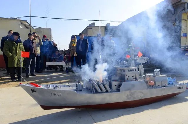 Residents look on as a mocked missile, made of gunpowder, fires from a homemade replica of a destroyer vessel made by retired fishboat captain Guo Changhai, during a test run in Xiaojia village of Rizhao, Shandong province, December 13, 2014. (Photo by Reuters/China Daily)