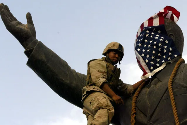 A U.S. Marine covers the face of a statue of Iraqi President Saddam Hussein with a U.S. flag in Baghdad, Iraq April 9, 2003. (Photo by Goran Tomasevic/Reuters)