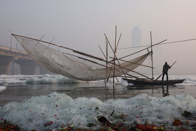 A fisherman on a boat stands next to a fishing net covered with foam, on the polluted Yamuna river, on a smoggy morning amid ongoing air pollution in New Delhi, India, on November 21, 2025. (Photo by Bhawika Chhabra/Reuters)