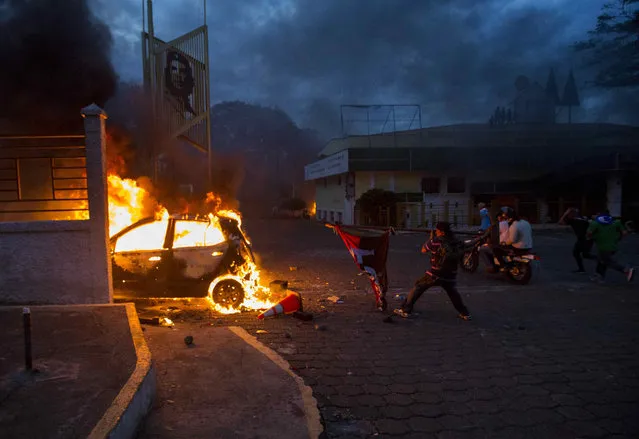 A man throws a flag of the current ruling party towards a burning vehicle as smoke rises from the Caruna Savings and Credit Cooperative headquarters during protests in Managua, Nicaragua, 30 May 2018. According to reports, at least 83 people have died in the ongoing socio-political crisis in Nicaragua since 18 April. (Photo by Jorge Torres/EPA/EFE)