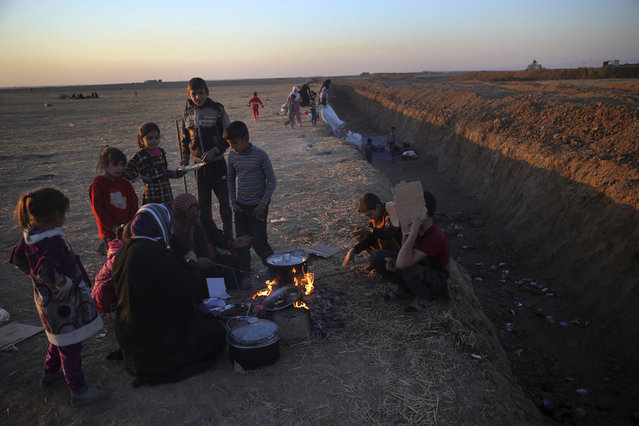 Iraqi women who fled with their families the fighting between Iraqi forces and Islamic State militants, sit on the ground and cook for their child, as they wait to cross to the Kurdish controlled area, in an open field in the Nineveh plain, northeast of Mosul, Iraq, Friday, November 18, 2016. Iraqi troops advanced cautiously into eastern districts of Mosul on Friday, facing stiff resistance from Islamic State militants a day after they paused their assault due to poor visibility, officers said. The pause also allowed the residents running out of food in areas liberated from IS to get some supplies from Iraqi troops and aid organizations. (Photo by Hussein Malla/AP Photo)