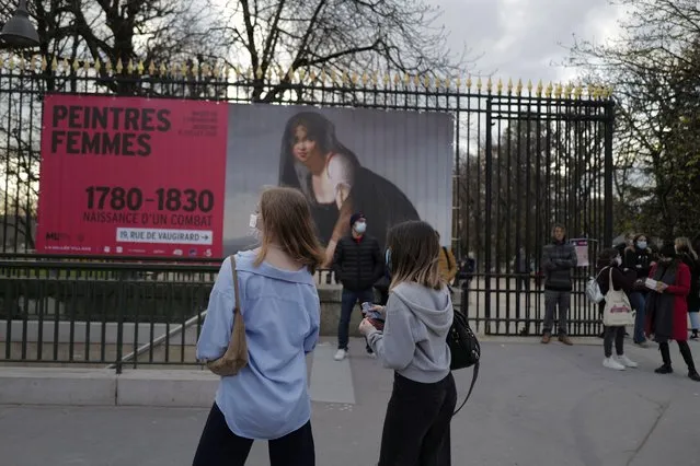 Woman gather at the entrance of the Luxembourg Garden, near a placard announcing a closed exhibition of Women Painters, in Paris, Sunday, March 21, 2021. The French government has backed off from ordering a tough lockdown for Paris and several other regions despite an increasingly alarming situation at hospitals with a rise in the number of COVID-19 patients. (Photo by Francois Mori/AP Photo)