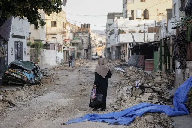 A Palestinian woman walks on a damaged road in the Jenin refugee camp in the West Bank, Wednesday, July 5, 2023, after the Israeli army withdrew its forces from the militant stronghold. The withdrawal of troops from the camp ended an intense two-day operation that killed at least 13 Palestinians, drove thousands of people from their homes and left a wide swath of damage in its wake. One Israeli soldier was also killed. (Photo by Majdi Mohammed/AP Photo)