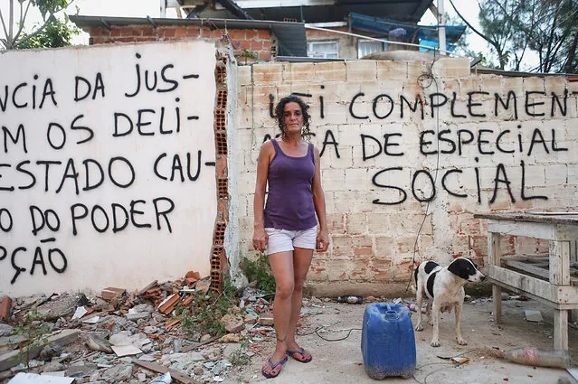 Longtime resident Sandra Maria de Sousa poses near her home in front of anti-demolition grafitti in the mostly demolished Vila Autodromo favela community, a former fishing colony, on January 6, 2016 in Rio de Janeiro, Brazil. Most residents of the favela community have moved out and had their properties demolished after receiving compensation for their homes which are located directly adjacent to the Olympic Park under construction for the Rio 2016 Olympic Games. (Photo by Mario Tama/Getty Images)