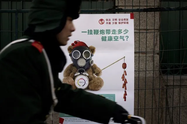 In this Friday, February 5, 2016 photo, a Chinese paramilitary policeman rides past a poster showing an image of masked teddy bear holding firecrackers with the words “A roll of firecracker carries off how many fresh air?” on display near the foreign embassies area in Beijing. (Photo by Andy Wong/AP Photo)