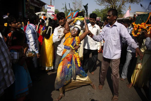 A woman devotee in trance with her tongue pierced with a metal rod, is helped by men on her way to a temple of Lord Murugan, on the occasion of Panguni Uthiram festival, in Ahmadabad, India Friday, April 3, 2015. One of the most important festival of southern India, which is  observed in the Tamil month of Panguni. (Photo by Ajit Solanki/AP Photo)