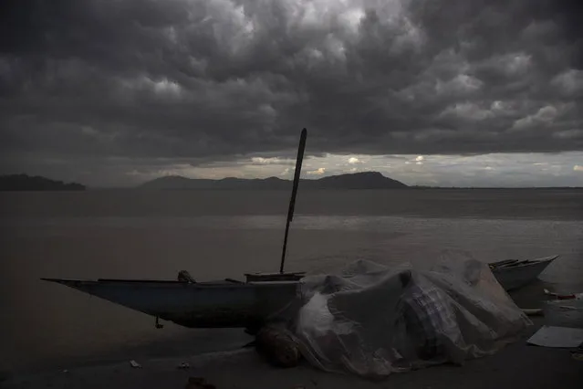 Fishermen under a plastic sheet cover themselves from rain near their boat as the monsoon cloud hover over the river Brahmaputra in Gauhati, India, Friday, July 23, 2021. Brahmaputra is one of Asia's largest rivers, which passes through China's Tibet region, India and Bangladesh before converging into the Bay of Bengal. (Photo by Anupam Nath/AP Photo)