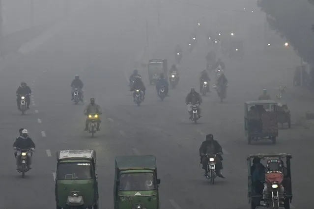 Commuters make their way along a street amid dense smog in Lahore on December 18, 2023. (Photo by Arif Ali/AFP Photo)