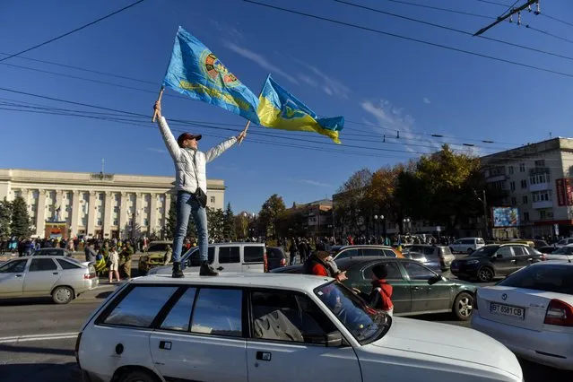 People wave Ukrainian flags atop a car during a patriotic rally after Presidnet Zelesnky's visit to the recaptured city of Kherson, Ukraine, 14 November 2022. Ukrainian troops entered Kherson on 11 November after Russian troops had withdrawn from the city. Kherson was captured in the early stage of the conflict, shortly after Russian troops had entered Ukraine in February 2022. (Photo by Oleg Petrasyuk/EPA/EFE)