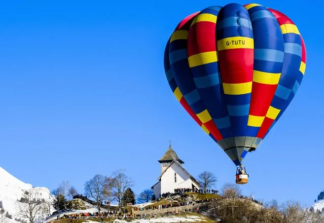 A hot-air balloon flies over a church during the 44th International Hot Air Balloon Festival in Chateau-d'Oex, Switzerland, Saturday, January 20, 2024. (Photo by Jean-Christophe Bott/Keystone via AP Photo)