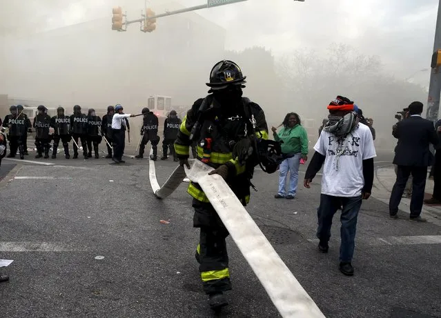 A Baltimore firefighter pulls a hose through crowds of protestors, who later cut the hose, in front of a burning building during clashes in Baltimore, Maryland April 27, 2015. (Photo by Jim Bourg/Reuters)