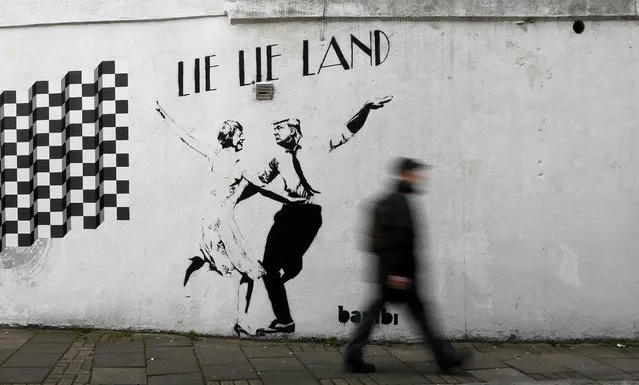 A pedestrian passes a new piece of art by street artist Bambi in London. in London, Thursday, February 16, 2017. The work, entitled Lie Lie Land, features a dancing British Prime Minister Theresa May and President Donald Trump in the pose made famous by the movie La La Land. (Photo by Kirsty Wigglesworth/AP Photo)