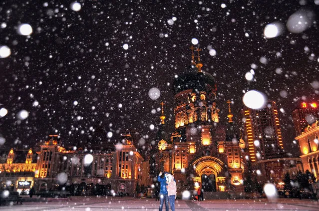 This photo taken on November 7, 2021 shows people taking photos in front of the Saint Sophia Cathedral during a snowfall in Harbin in China's northwastern Heilongjiang province. (Photo by AFP Photo/China Stringer Network)