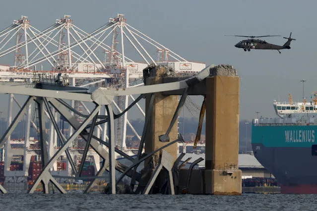 A helicopter flies near the Francis Scott Key Bridge, after the Dali cargo vessel crashed into it causing it to collapse, in Baltimore, Maryland, U.S., March 26, 2024. (Photo by Julia Nikhinson/Reuters)