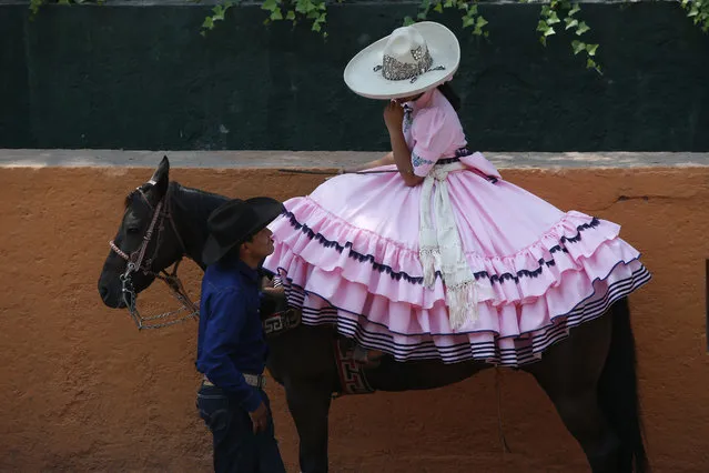 A cowboy chats with an Escaramuza before her presentation at the Rancho del Charro on the outskirts of Mexico City, Mexico, Saturday, May 18, 2019. Mexico's Charros National Association is marking their 98th anniversary, celebrated from May 15 -June 2. (Photo by Ginnette Riquelme/AP Photo)
