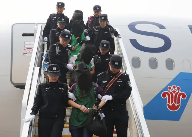 Police escort a group of people wanted for suspected fraud in China, after they were deported from Kenya, as they get off a plane after arriving at Beijing Capital International Airport in Beijing, China, April 13, 2016. (Photo by Yin Gang/Reuters/Xinhua)