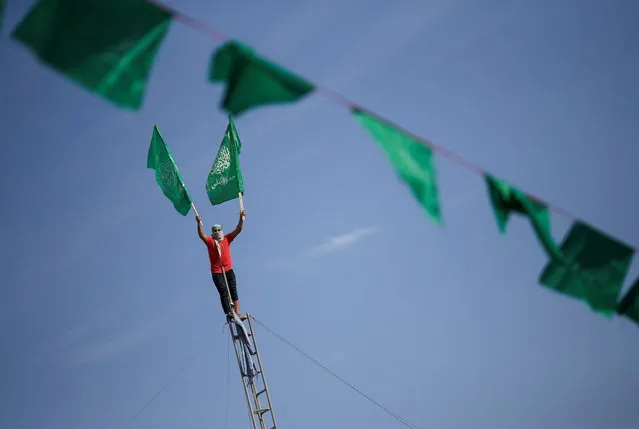 Bunting hangs as a Palestinian holds flags on a ladder at a rally marking the 34th anniversary of Hamas' founding, in the northern Gaza Strip on December 10, 2021. (Photo by Mohammed Salem/Reuters)