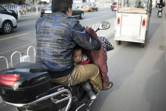 A man transports his son on a scooter along a road in Beijing, China on April 18, 2016. (Photo by Fred Dufour/AFP Photo)