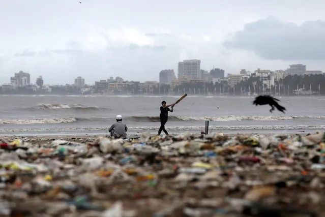 A boy plays cricket next to garbage on the Juhu beach in Mumbai, India, July 10, 2019. (Photo by Francis Mascarenhas/Reuters)
