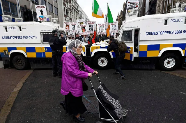 A woman pushes her shopping trolley past armoured police vehicles seperating a counter demonstration from a demonstration by former British soldiers who served in Northern Ireland, in Belfast, April 14, 2017. (Photo by Clodagh Kilcoyne/Reuters)