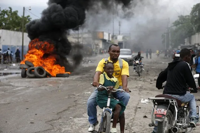 A father carries his daughter on a bicycle past a burning barricade during a protest against the ratification of interim Prime Minister Jean Michel Lapin, in Port-au-Prince, Haiti, Thursday, May 30, 2019. (Photo by Dieu Nalio Chery/AP Photo)