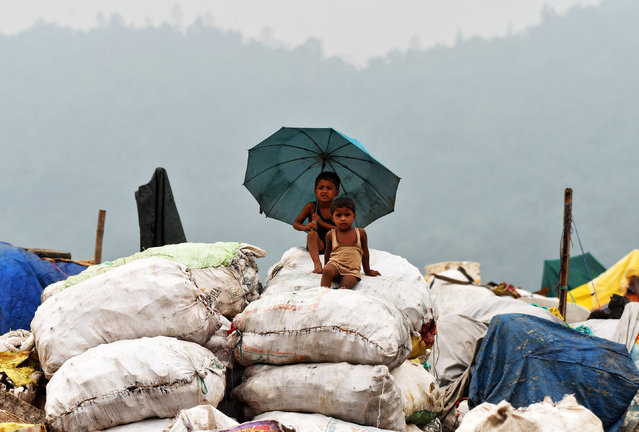 Children shelter under an umbrella during rain as they sit on sacks filled with recyclable material at a garbage dumping site on the eve of World Environment Day, in Guwahati, India June 4, 2017. (Photo by Anuwar Hazarika/Reuters)