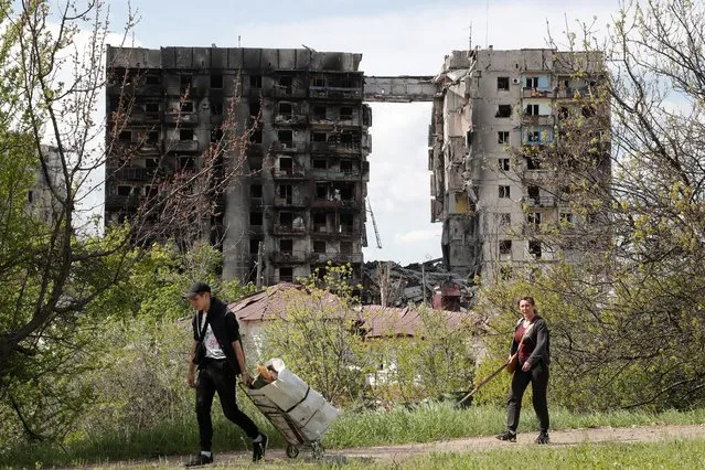 People walk near a residential building destroyed during Ukraine-Russia conflict in the southern port city of Mariupol, Ukraine on May 3, 2022. (Photo by Alexander Ermochenko/Reuters)