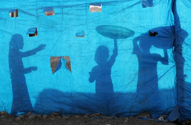 The silhouettes of Iraqi children are seen on tarpaulin as they collect water from a tank at the Al-Khazir camp for internally displaced people, located between Arbil and Mosul, on June 6, 2017. Hundreds of thousands of people have fled their homes as Iraqi forces press a massive operation to retake Mosul from the Islamic State jihadist group. (Photo by Karim Sahib/AFP Photo)