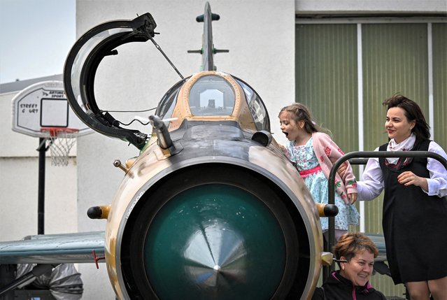 Visitors climb aboard of a MIG-21 Lancer displayed for the audience during ceremonies organized by the Romanian Minister of Defence at “Air Base 86 Borcea” in Borcea, Romania on May 15, 2023. Romania on May 15, 2023 officially retired its fleet of MiG-21s – a heritage from the Soviet era – as the NATO member and Ukraine neighbour is aiming to modernise its armed forces. Romania now uses a squadron of 17 F-16 fighter jets bought recently from Portugal, and signed a contract with Norway in November to buy 32 additional used F-16s. (Photo by Daniel Mihailescu/AFP Photo)