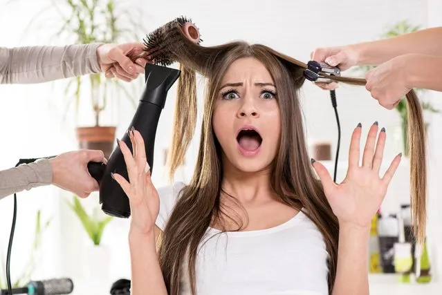 Shocked woman straightening long brown hair with hair dryer and round brush and hair irons at the hairdresser. (Photo by Milan Markovic/Getty Images)