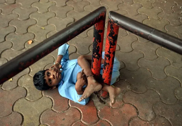 In this photograph taken on May 20, 2014 nine year old Indian boy Lakhan Kale is tied with a cloth rope around his ankle, to a bus-stop pole in Mumbai. (Photo by Punit Paranjpe/AFP Photo)