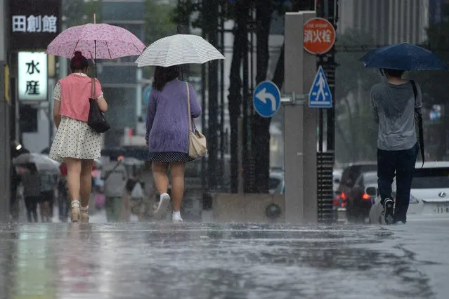People walk on the street under the sudden rain at Ginza shopping district in Tokyo on June 29, 2014. Many shoppers on June 29 took refuge from the shower in nearby shops and department stores. (Photo by Toru Yamanaka/AFP Photo)
