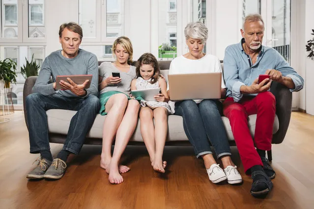 Group picture of three generations family sitting on one couch using different digital devices. (Photo by Westend61/Getty Images)