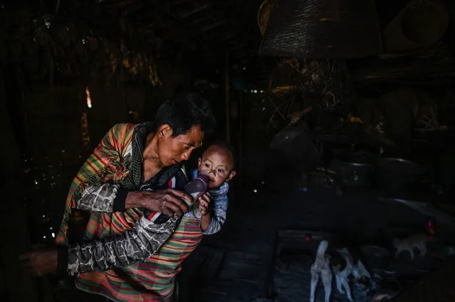 This photo taken on February 5, 2020 shows a man taking care of his child as his wife carries wood for the upcoming overnight ceremony by Naga tribeswomen to bless the harvest in Satpalaw Shaung village, Lahe township in Myanmar's Sagaing region. (Photo by Ye Aung Thu/AFP Photo)