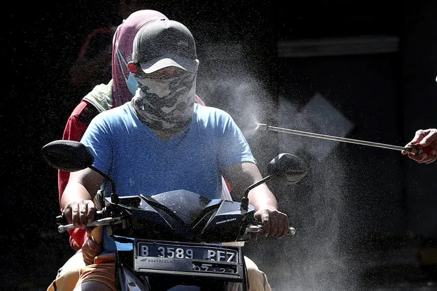 Motorists are sprayed with disinfectant in an attempt to curb the spread of coronavirus outbreak at the gate of a housing complex in South Tangerang, Indonesia, Tuesday, March 31, 2020. Indonesia will close its doors to foreign arrivals in an attempt to curb the coronavirus spread while the country plans to bring home more than a million nationals working abroad. (Photo by Tatan Syuflana/AP Photo)