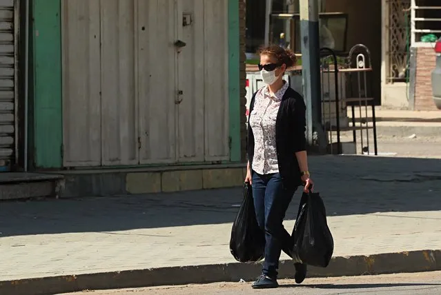 A masked woman walks past shops that are shuttered to help prevent the spread of the coronavirus during a curfew to help fight the spread of the coronavirus a nearly empty popular market in Baghdad, Iraq, Saturday, April 4, 2020. (Photo by Hadi Mizban/AP Photo)