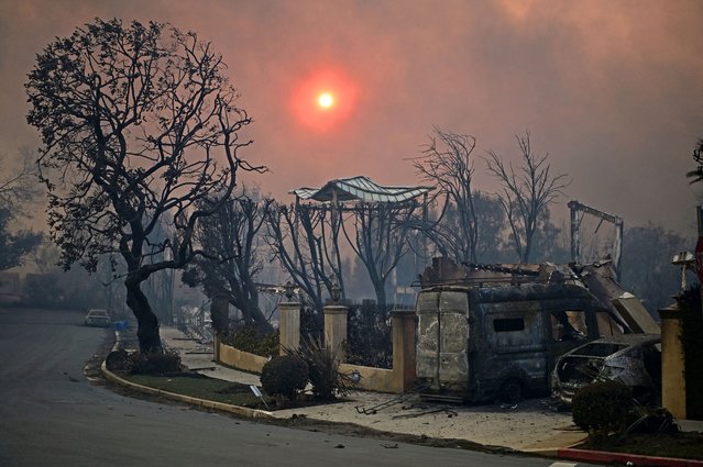 The sun is seen behind smoke above charred structures and vehicles after the passage of the Palisades Fire in Pacific Palisades, California, on January 8, 2025. At least five people have been killed in wildfires rampaging around Los Angeles, officials said on January 8, with firefighters overwhelmed by the speed and ferocity of multiple blazes. (Photo by Agustin Paullier/AFP Photo)