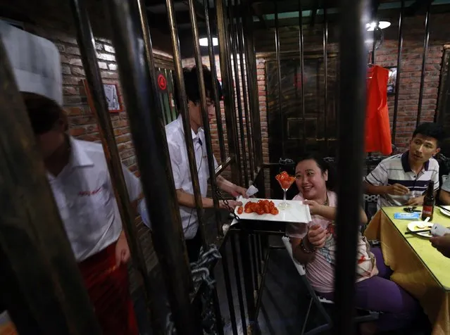 A customer receives a dish between iron bars as she eats a dinner at a jail-themed restaurant in the Chinese port city of Tianjin September 9, 2014. (Photo by Kim Kyung-Hoon/Reuters)