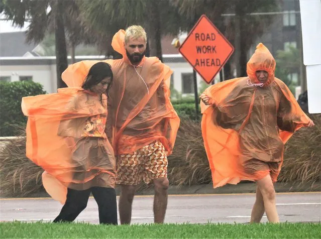 People in raincoats walk along International Drive in Orlando, Fla., Wednesday, September 28, 2022, as the first effects of Hurricane Ian are felt in central Florida. (Photo by Joe Burbank/Orlando Sentinel via AP Photo)